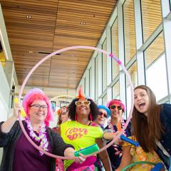 A group of students in colourful clothing posing with a hoola-hoop